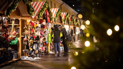 Internationella julmarknaden i Helsingfors. Juliga små försäljningsstånd och kunder som tittar på varor med ryggen mot kameran.