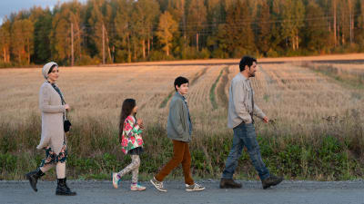 Familjen Mehdipour på promenad mot bakgrunden av en finländsk åker i solnedgången.