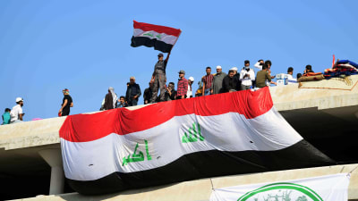 Irakier står på mur och håller upp flagga.