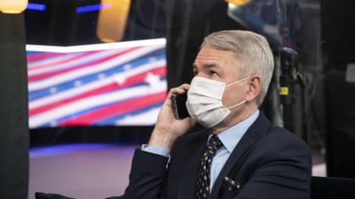Utrikesminister Pekka Haavisto talar i telefonen iklädd ansiktsskydd