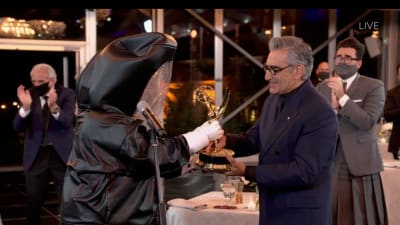 Eugene Levy tar emot sin Emmystatyett av en prisutdelare som klätt in i en heltäckande kostym för att minimera smittorisk för coronaviruset.