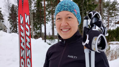 En kvinna klädd för skidåkning håller i skidor och stavar.