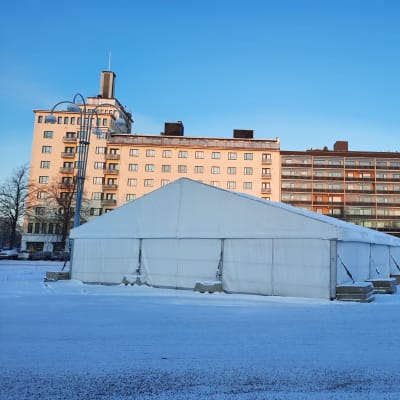 Valkoinen teltta Kotkan linja-autoasemalla, jonka aukion reunalla on korkeita kerrostaloja.
