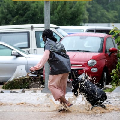 En kvinna med en väska på släp tar sig över en översvämmad parkeringsplats. Vattnet når till hennes anklar.