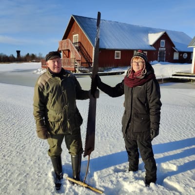 En man och en kvinna håller i en stor såg som förr användes för att såga isblock.