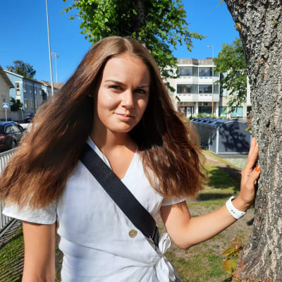 En kvinna står ute i en park intill ett träd