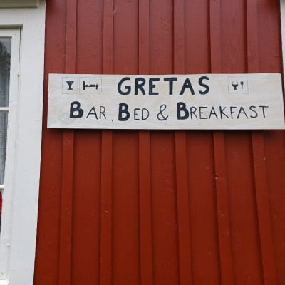 En skylt på ett rött trähus med texten Gretas bar, bed & breakfast