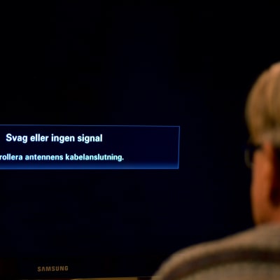 En man tittar på en tv där det på skärmen står "Svag eller ingen signal".