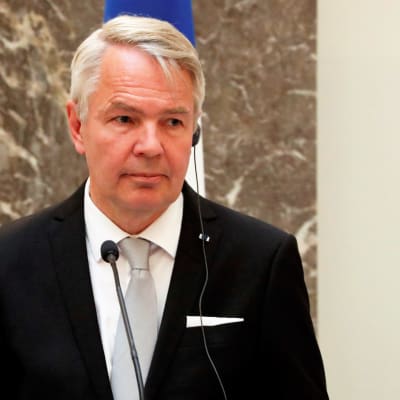 Pekka Haavisto mustassa puvussa, helmenharmaassa kravatissa. Taustalla näkyy Suomen lippu.