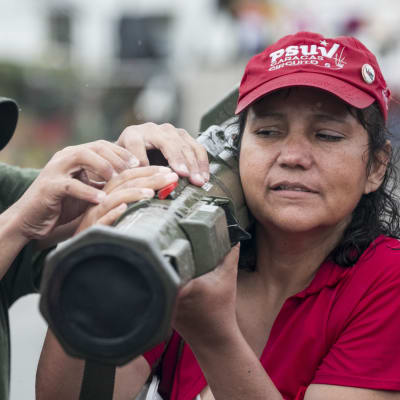 En kvinna håller i ett vapen på sin axel medan en man hjälper till i Caracas den 26 augusti. Både militära och civila deltog i Venezuelas militärövning.