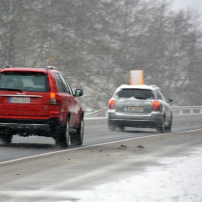 Två bilar kör på en väg som är slaskig. Diket är vitt av snö.