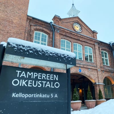 Luminen kyltti ”Tampereen oikeustalo” punatiilisen rakennuksen edustalla.