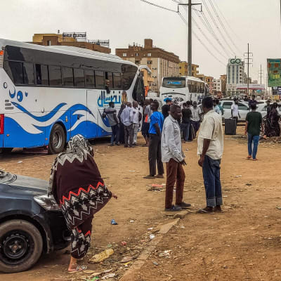 Ihmiset odottavat matkatavaroiden kanssa Khartumista lähtevää bussia.