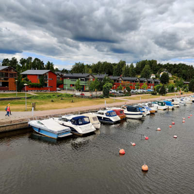 Båtar som gubbar i en å på rad intill en stenmur.