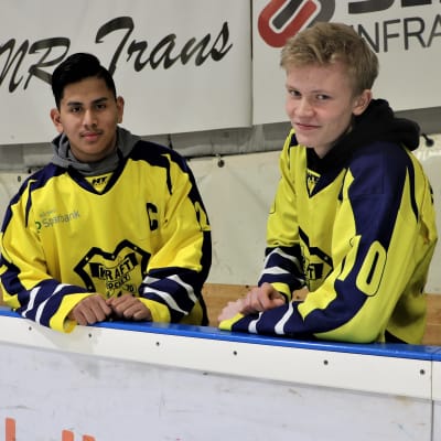 Lucas Nordgren och Linus Böling, hockeyspelare i Närpeslaget Krafts C-juniorer, står i ishallen vid sargen i gula spelskjortor