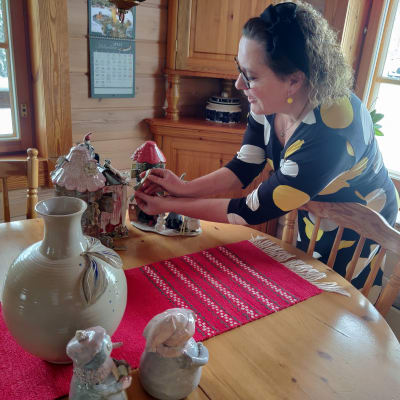 En kvinna står vid ett bord och fixar med tre små hus i keramik. Hon heter Nina Barrett.