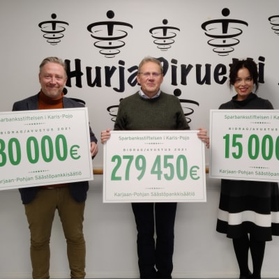 Tre personer håller upp skyltar med siffror som visar hur mycket understöd som en sparbanksstiftelse delat ut.