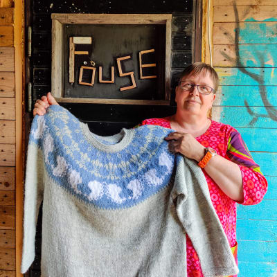 En kvinna håller upp en stickad tröja framför en dörr.