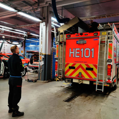 En man står och ser på en annan man som sitter på taket till en brandbil.