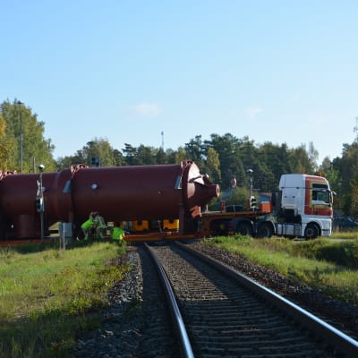 En långtradare står rakt över en järnvägsövergång. Två brandmän står vid ena sidan av fordonet.