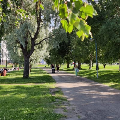Kävelijöitä kesäisessä jokimaisemassa.