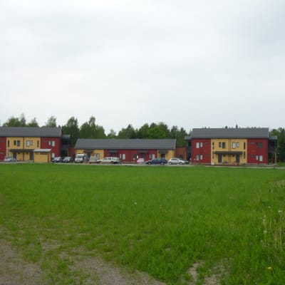 Tre rödgula hus med träfasad, en grön gräsplan i förgrunden.