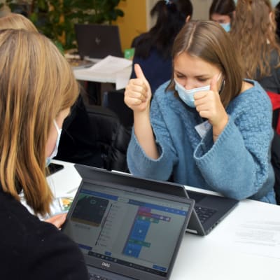 Flickor vid datorer, en håller upp båda tummarna som ett tecken på att nåt lyckades.