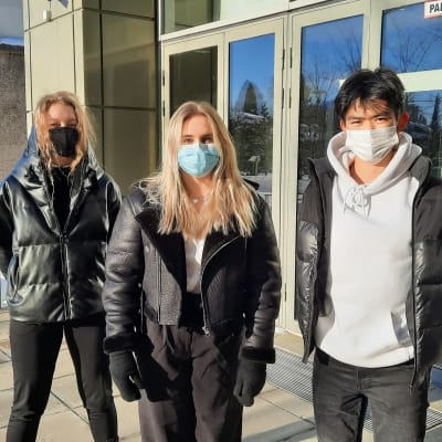 Tre ungdomar med munskydd står utanför en skolbyggnad.
