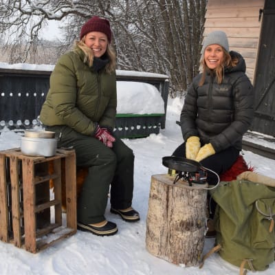Två leende kvinnor i vintrig miljö vid ett stormkök