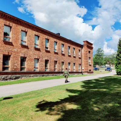 En kvinnlig beväring går på en väg längs en byggnad.
