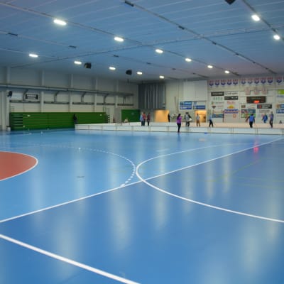 En idrottshall med blått golv. Elever spelar innebandy i bortre ändan av salen.