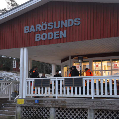 Ett rött hus, Barösundsboden, som är en bybutik. Folk står utanför huset på en takförsedd stor altan 