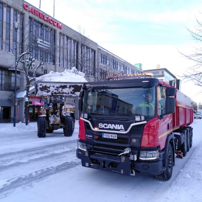 Traktori nostaa lunta kuorma-auton kyytiin.