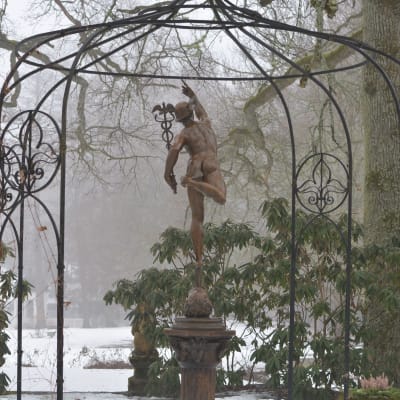 En skulptur av en man som pekar fingret mot himlen som står i en fontän i ett vinterlandskap.