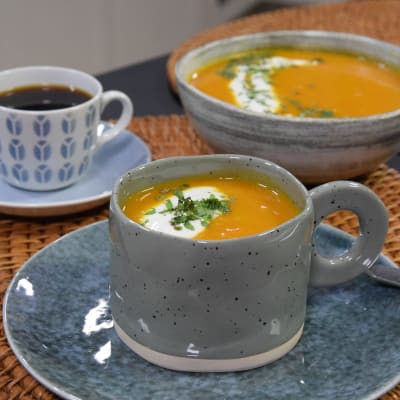 Portioner med morotsoppa och en kopp med kaffe på ett bord