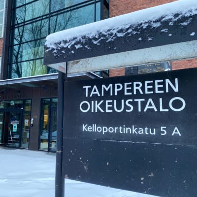 Luminen kyltti ”Tampereen oikeustalo” punatiilisen rakennuksen edustalla.