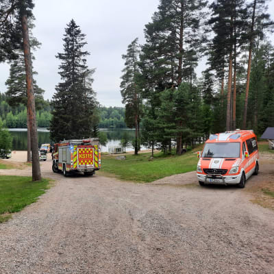 Pelastuslaitoksen kenttäjohtoauto, paloauto ja poliisiauto uimarannan alueella.