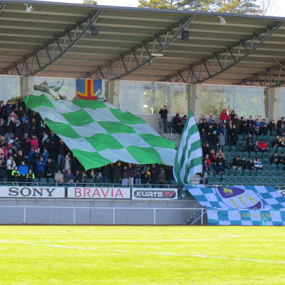 IFK Mariehamn-supportrar på läktare med grönvit flagga.