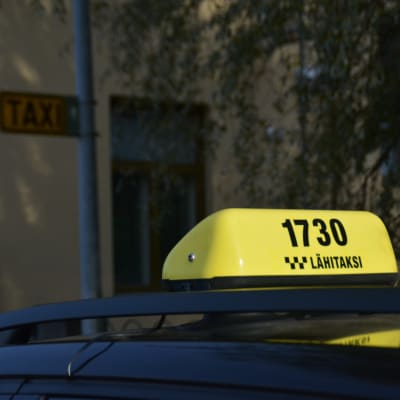 En gul taxiskylt på en taxibil.