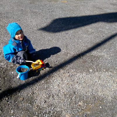 Fyraårig pojke leker med hink och lastbil i gruset.