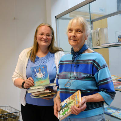 Irmelin Sandman-Lilius och Suzanne "Muddle" Lilius står med böcker i händerna i Hangö bibliotek.