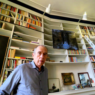 Författaren Jörn Donner står framför hög bokhylla med stege