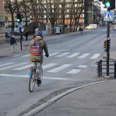 En cyklist med färggrann ryggsäck cyklar över Aurabron mot Åbo centrum.