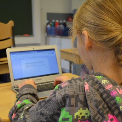 En flicka sitter i en skolbänk och skriver på sin lärplatta.