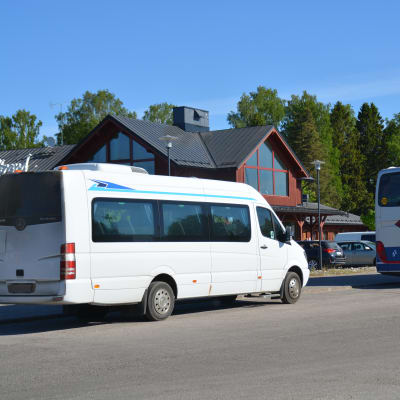 En större taxi och en buss står parkerade vid en affärsfastighet i rött trä.