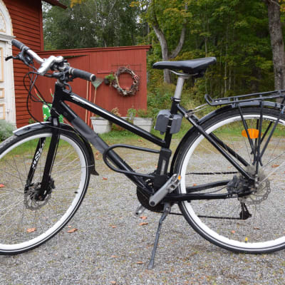 En svart hybridcykel av dammodell som står parkerad på en grusplan.
