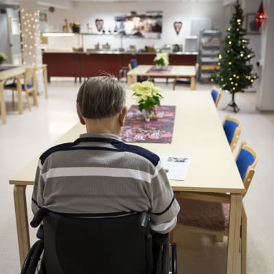 En äldre man sitter i rullstol vid ett bord på ett servicehem. 