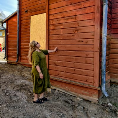En kvinna står och haller handen på en röd husvägg.
