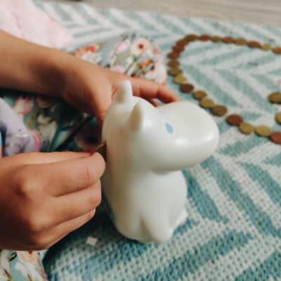 Ett barn lägger in mynt i en Mumin-formad spargris.