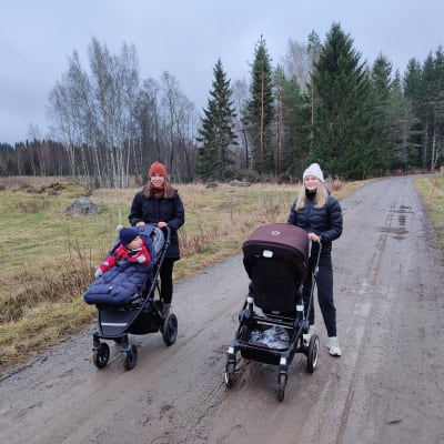 Sara och Erika står på en väg med sina barn i vagn.